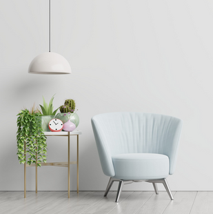 Blue chair in a well lit room surrounded by plants. A red clock on the table next to it.