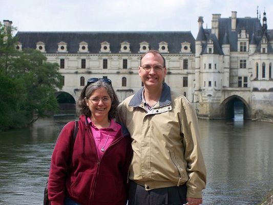 Smiling couple standing in front of a European-style castle over a river