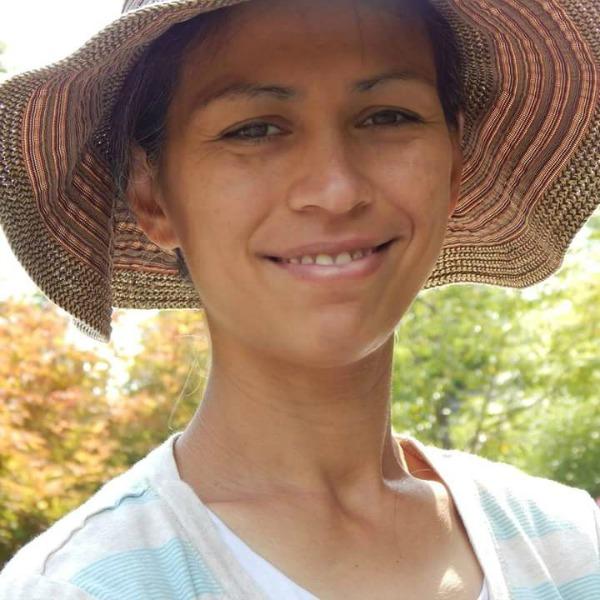 Smiling woman wearing a wide-brimmed hat and light striped shirt outdoors on a sunny day